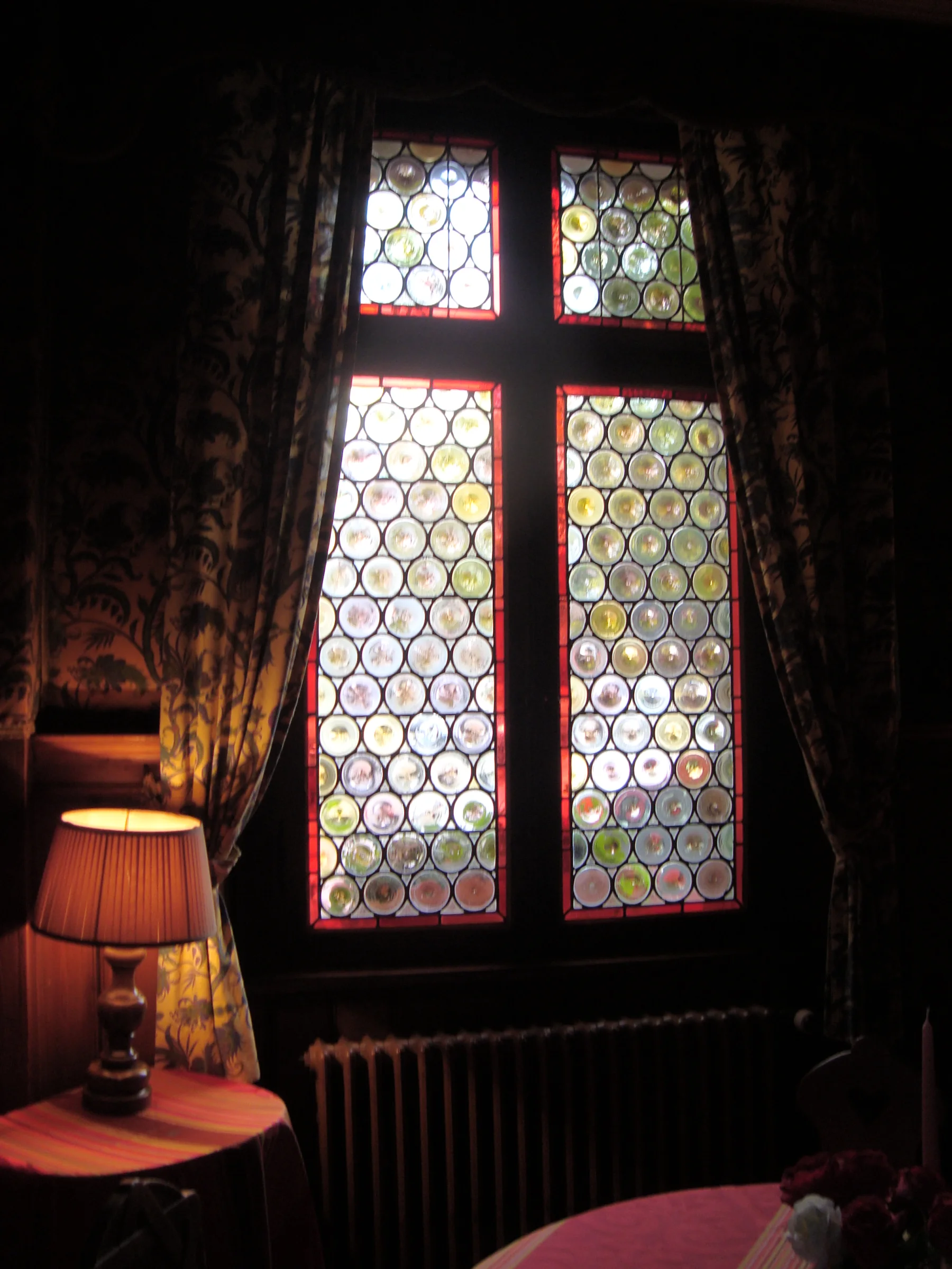 Des motifs circulaires et des touches de couleur rythment les panneaux d’une fenêtre dans son intérieur.