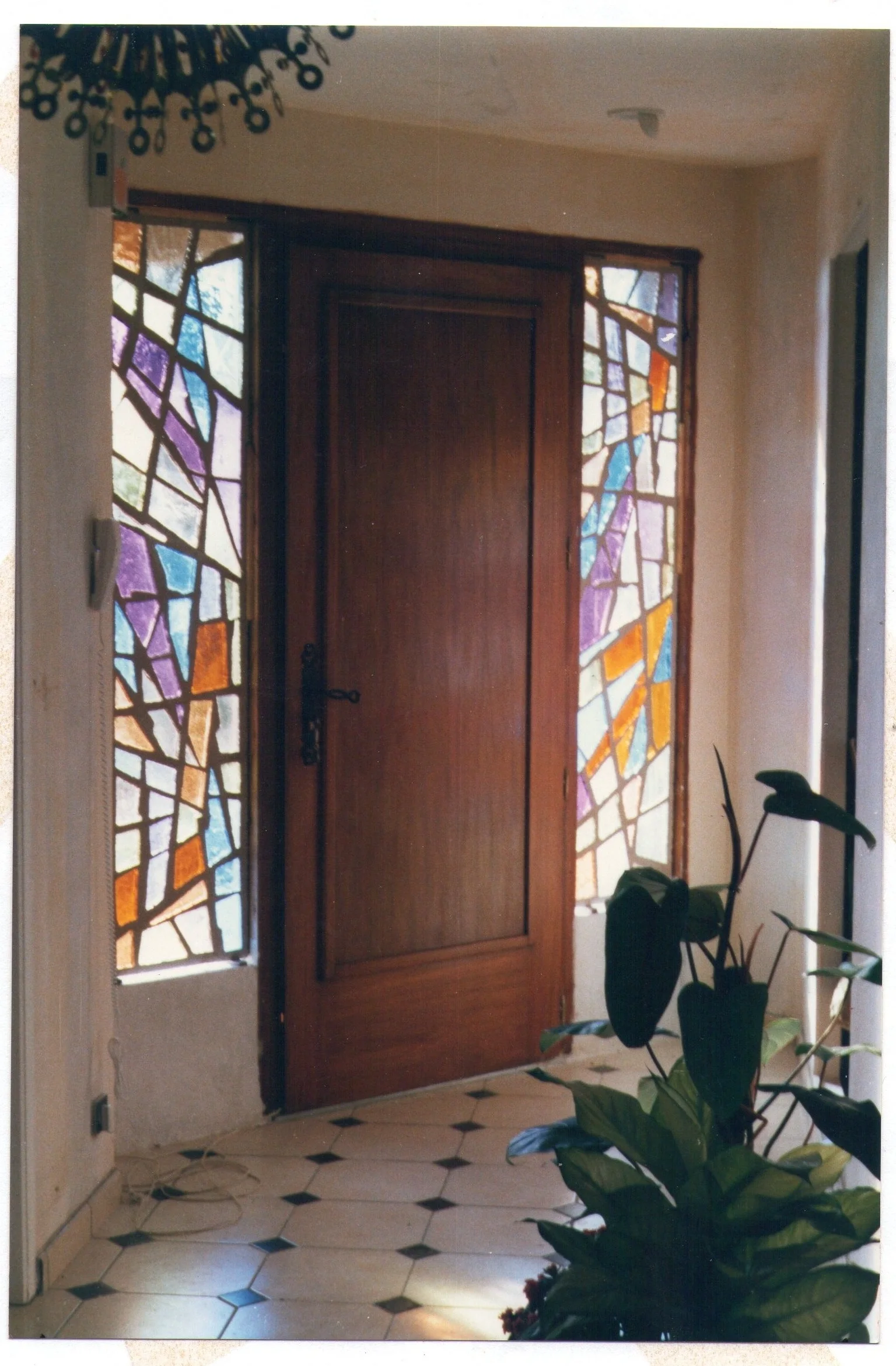 Des panneaux de verre coloré encadrent une porte d’entrée, avec des formes et des teintes variées.
