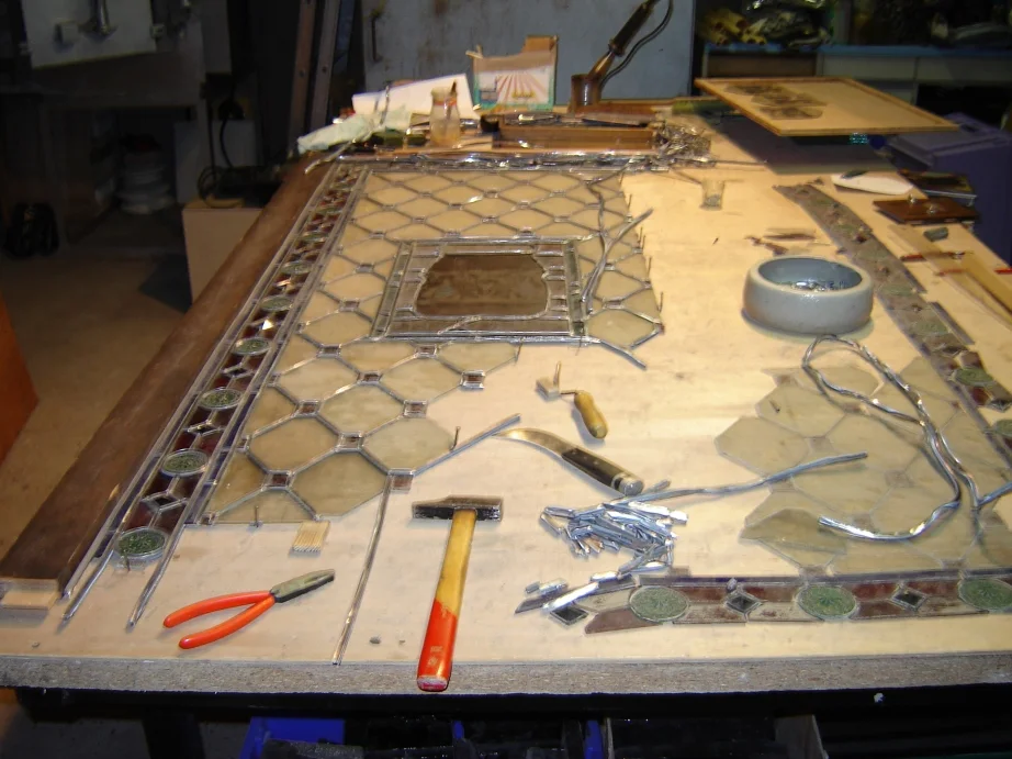 Un panneau de vitrail en cours de montage, posé sur une table avec les outils de l’atelier.