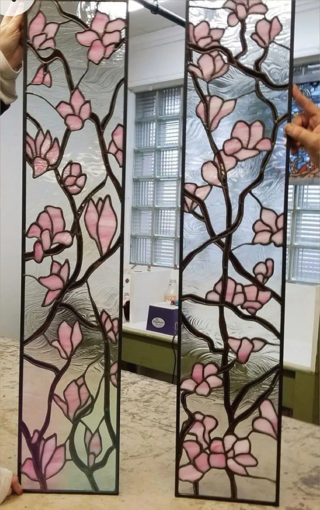 Des branches et des fleurs roses parcourent deux panneaux de verre présentés à l’atelier.
