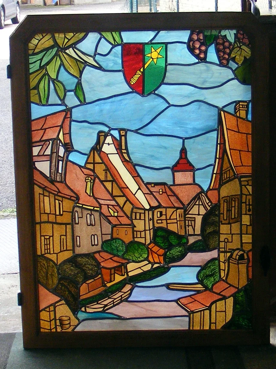 Une scène de ville en vitrail : façades colorées, toitures et cours d’eau sont réunis dans cette composition figurative.