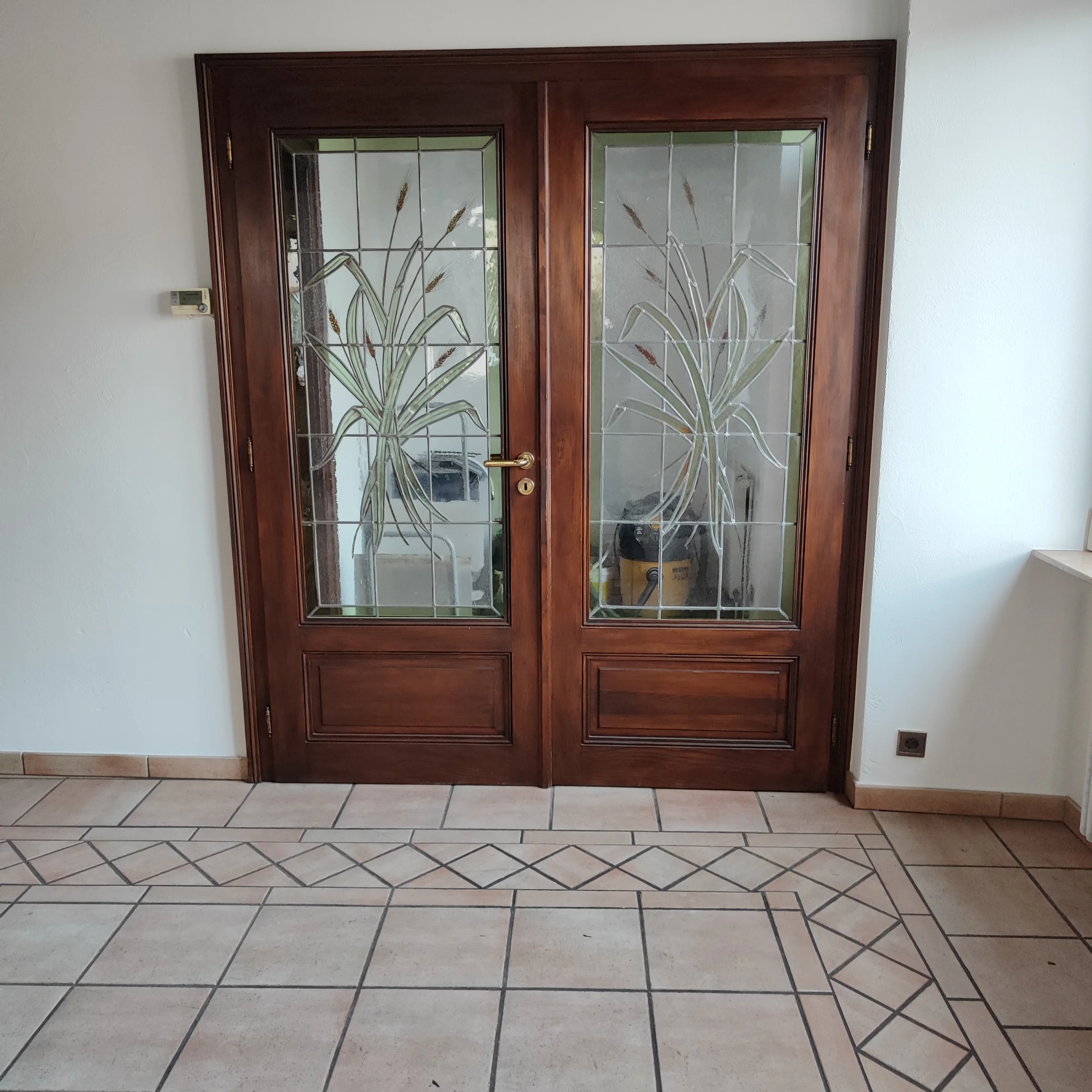 Deux panneaux de porte où des motifs végétaux se dessinent dans un verre clair, au sein d’un intérieur.